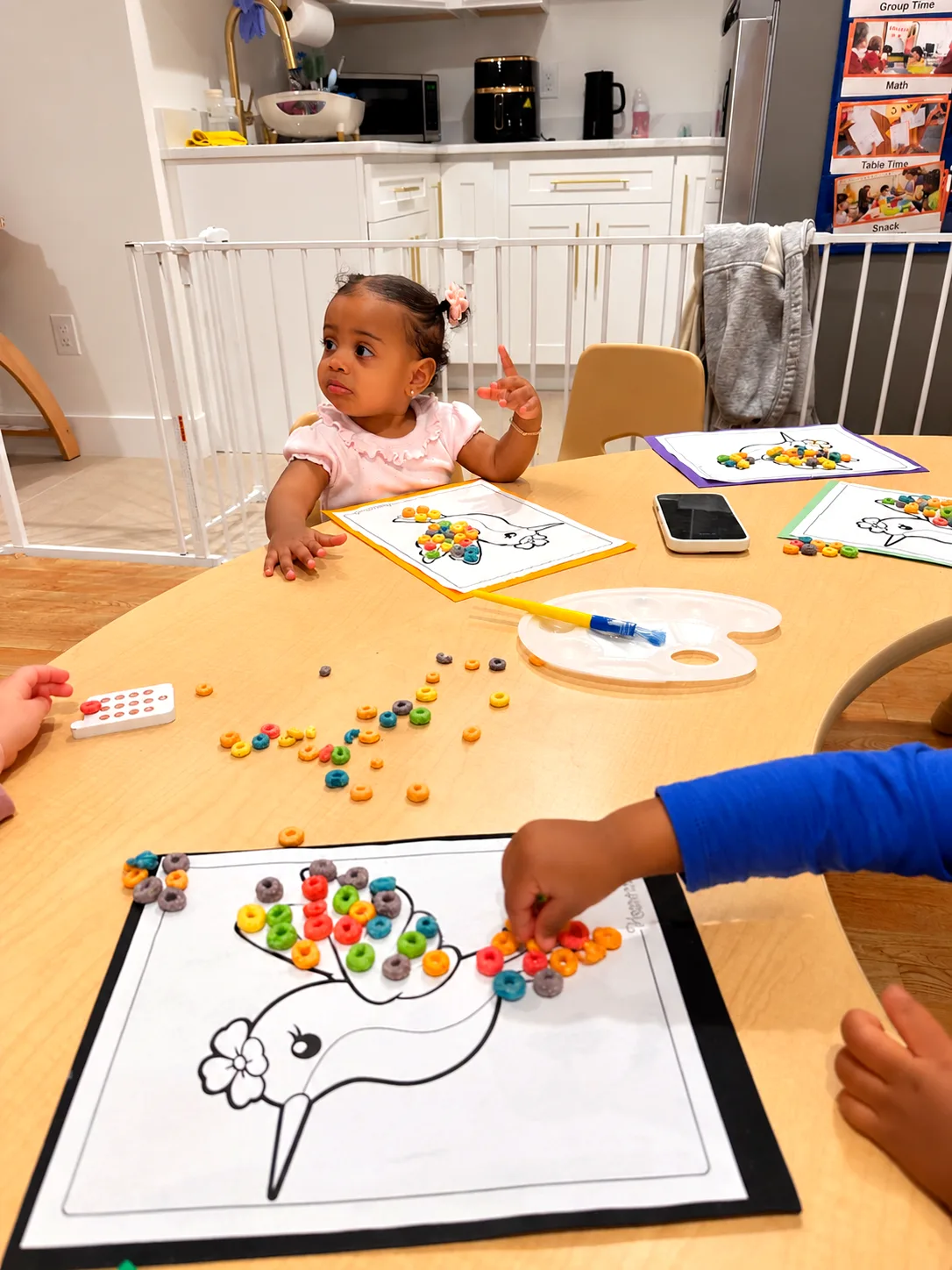 Children placing colorful cereal rings on unicorn coloring sheets during a table activity