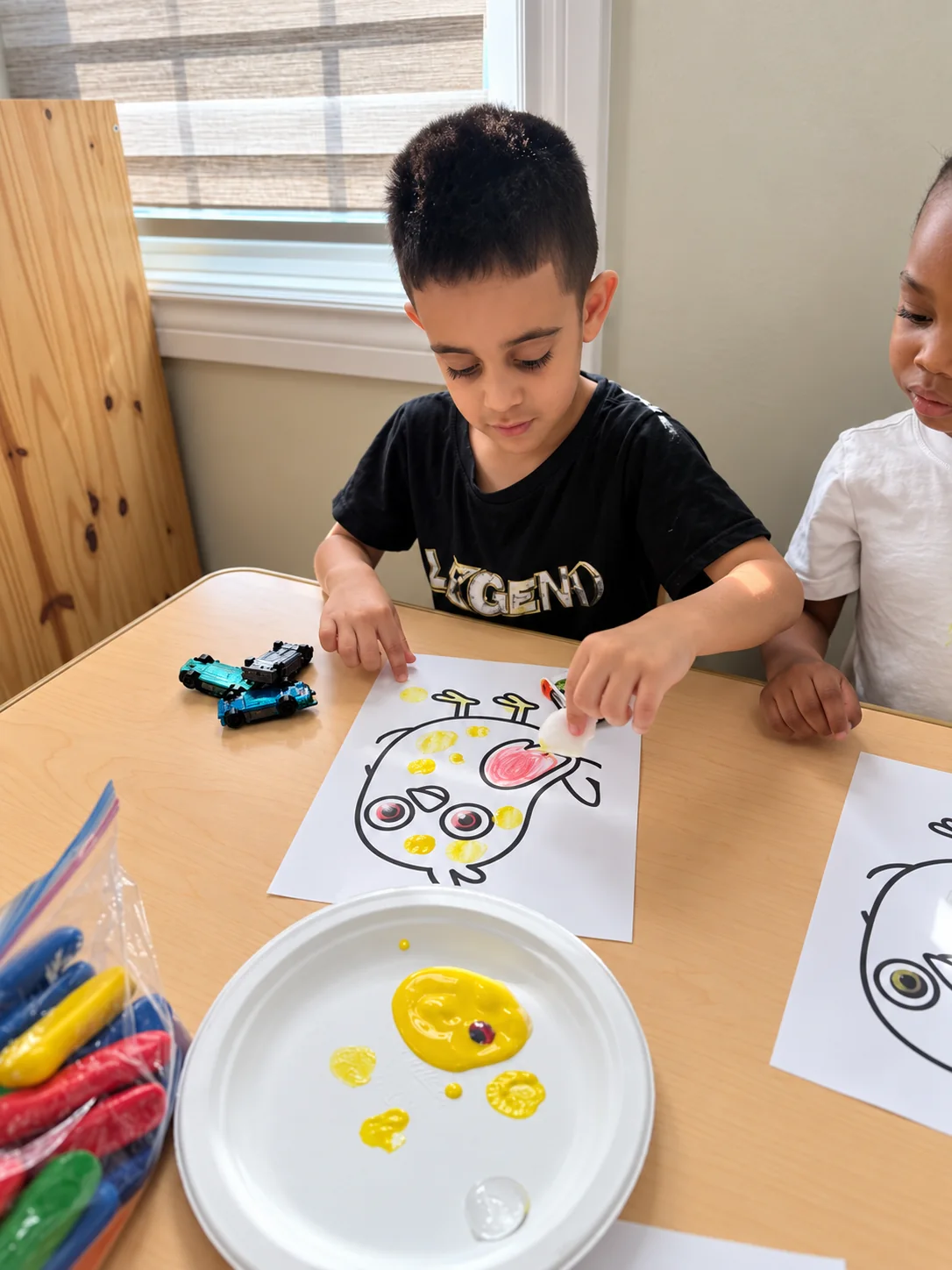 Child adding yellow fingerprints to a playful character art activity