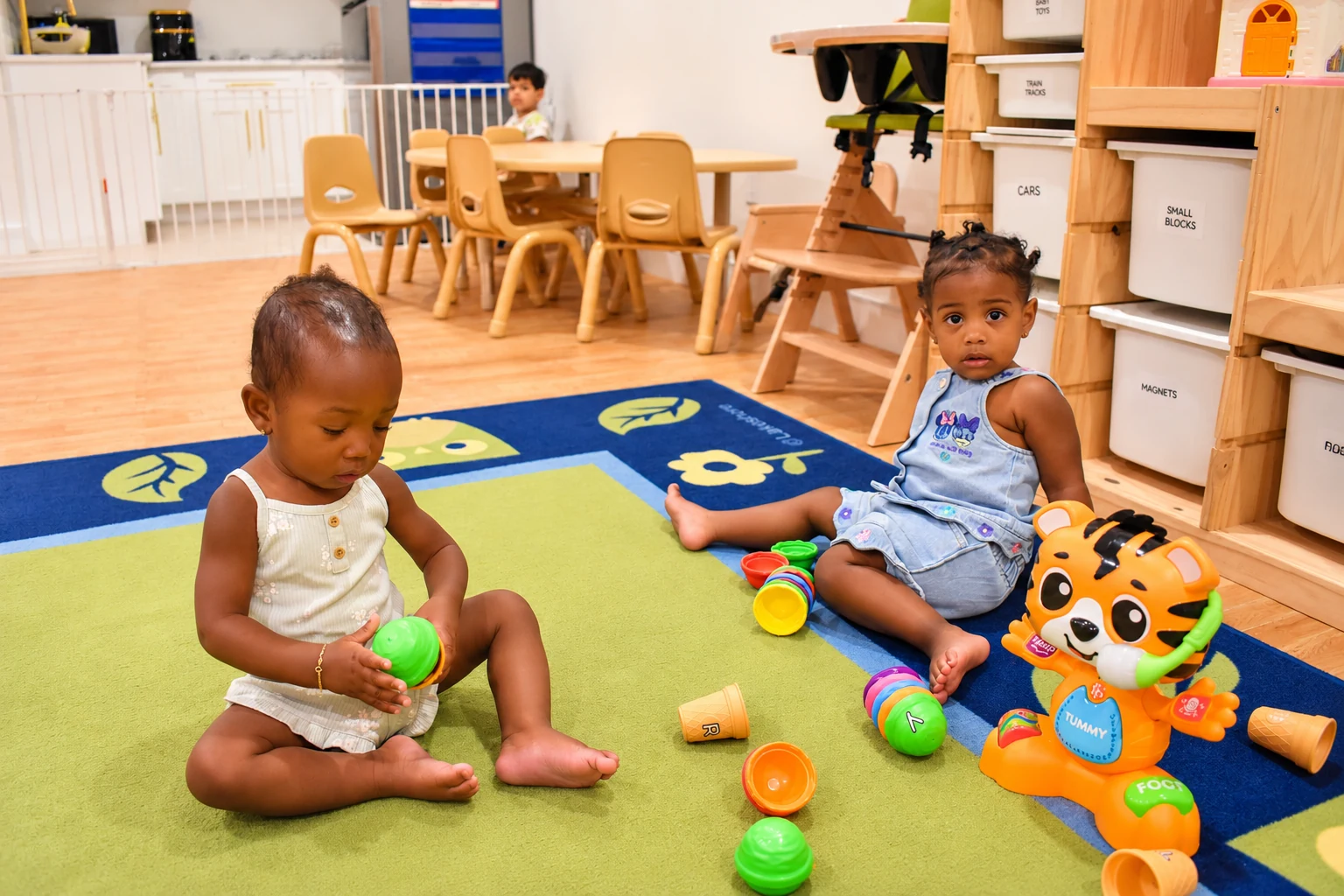 Toddlers exploring colorful stacking cups and toys on a soft classroom rug