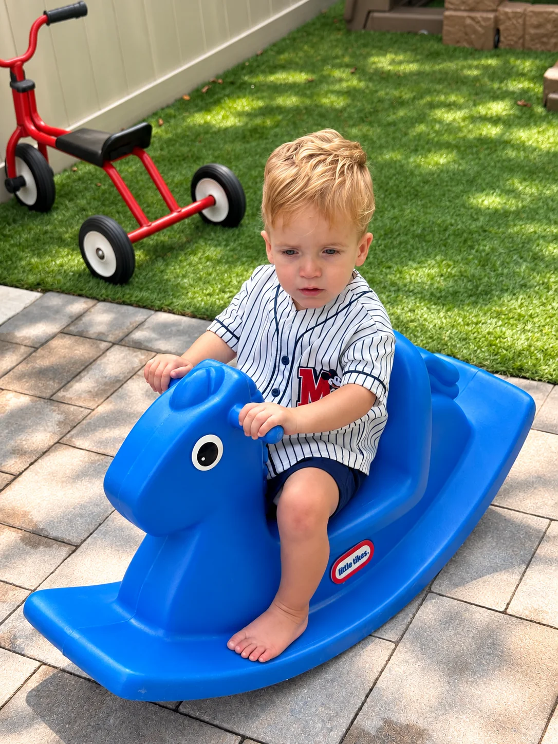 Toddler enjoying a blue rocking horse in the outdoor play area