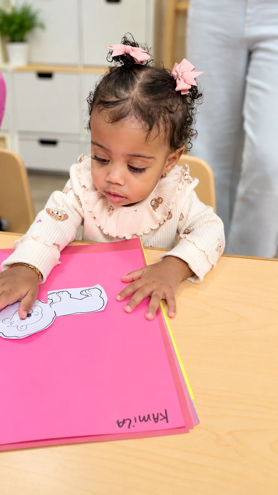 Young child arranging paper pieces on bright cardstock during a classroom art project