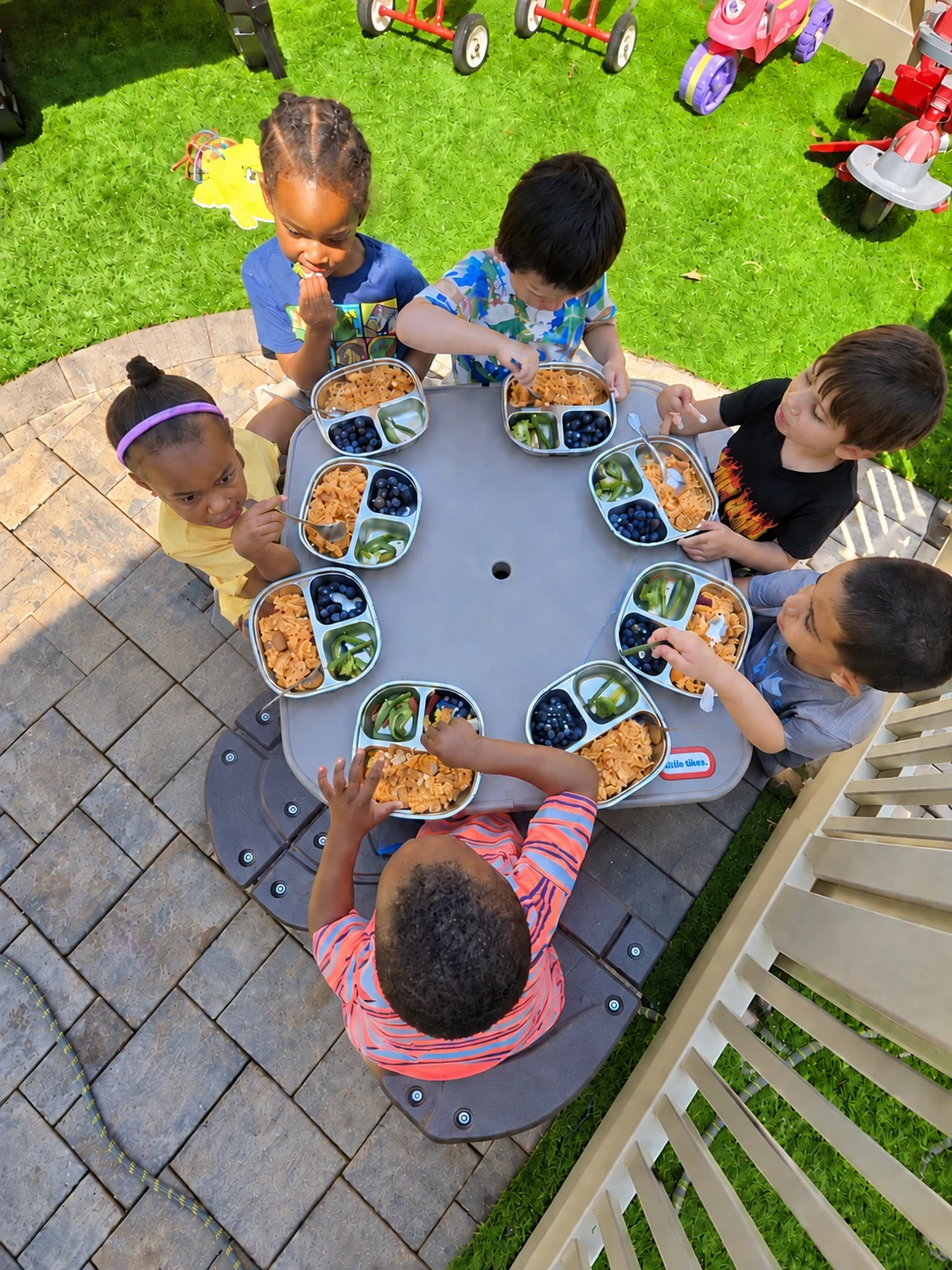 Children enjoy a balanced outdoor meal with pasta, blueberries, and fresh vegetables at Tina's Tiny Clubhouse