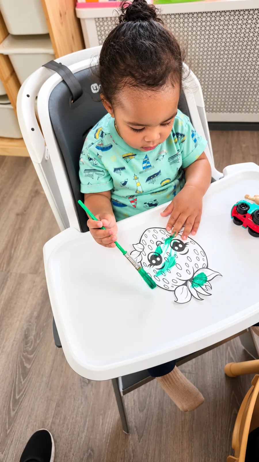Toddler painting a strawberry picture with a green paintbrush