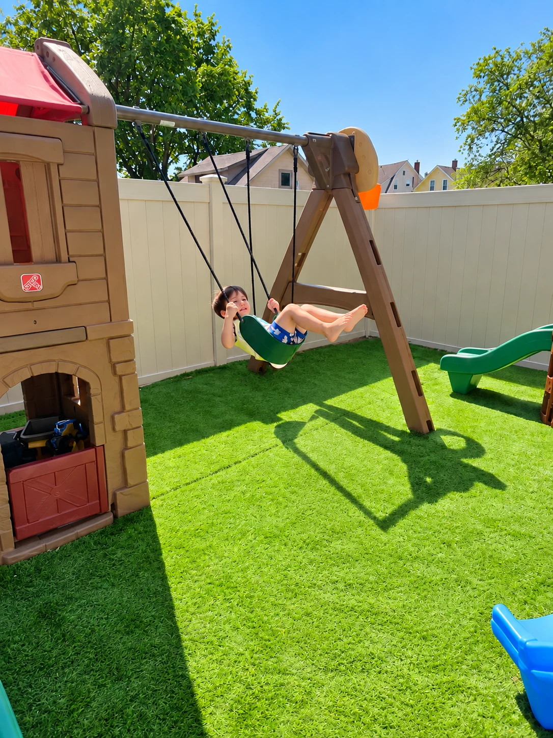 Child swinging in the fenced backyard play area on a sunny day