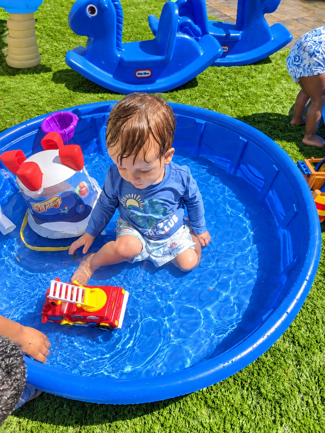 Toddler exploring water play in a small outdoor pool on a sunny day