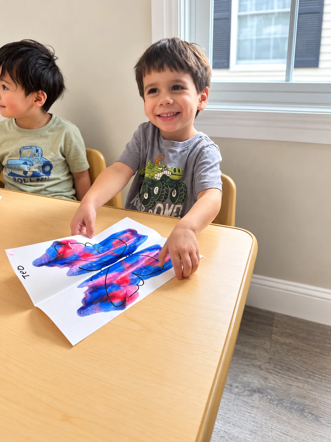 Smiling child showing a colorful butterfly painting during a classroom art activity