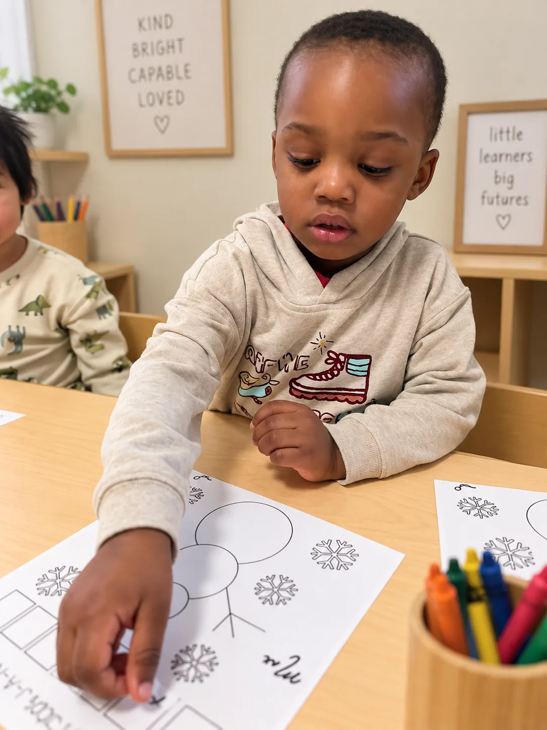 Child tracing a winter snowflake worksheet at a classroom table with crayons nearby