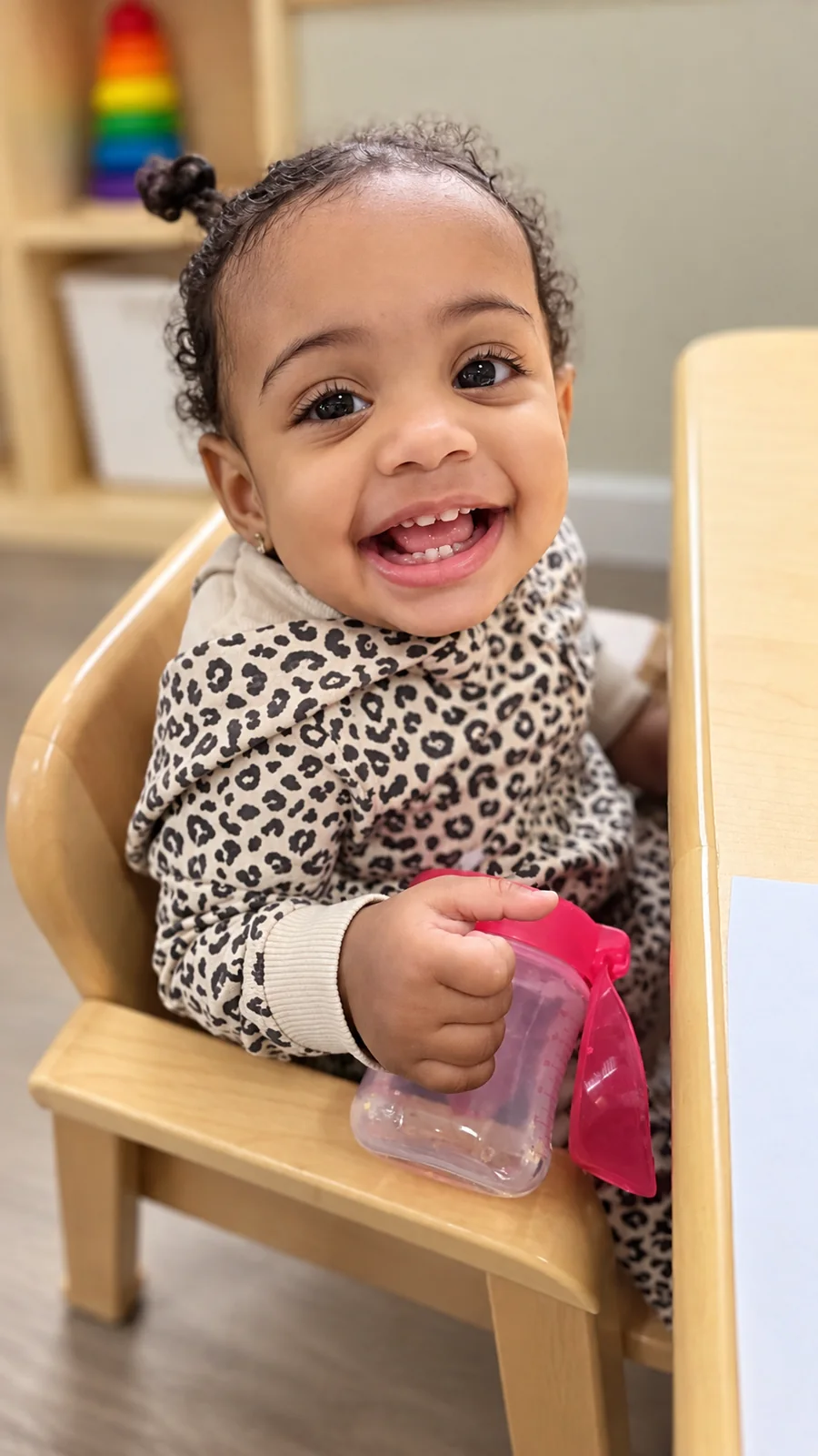 Smiling toddler seated at a classroom table during playtime