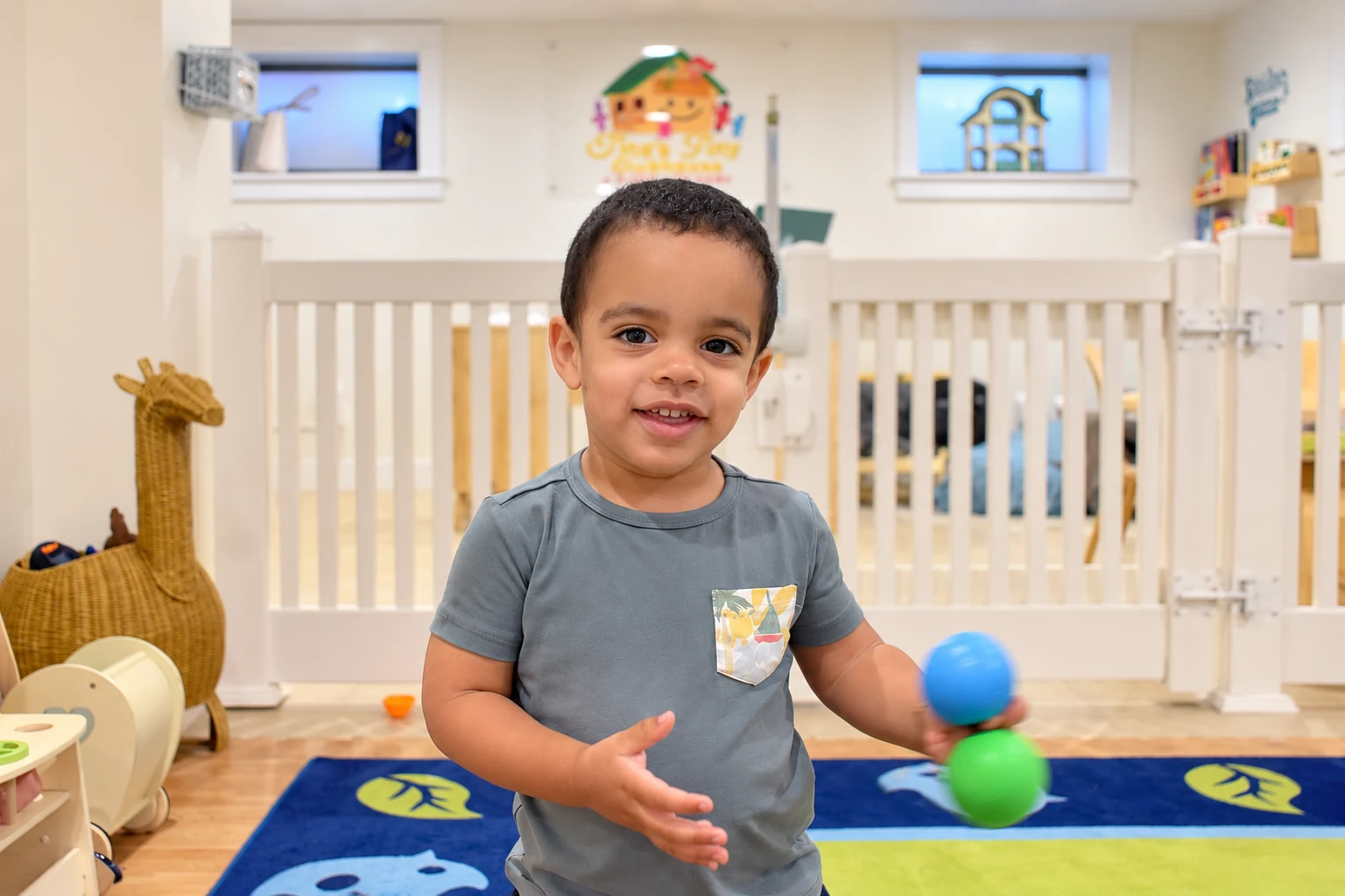 A smiling child holding colorful balls in a bright, warm playroom at Tina's Tiny Clubhouse in Freeport, NY
