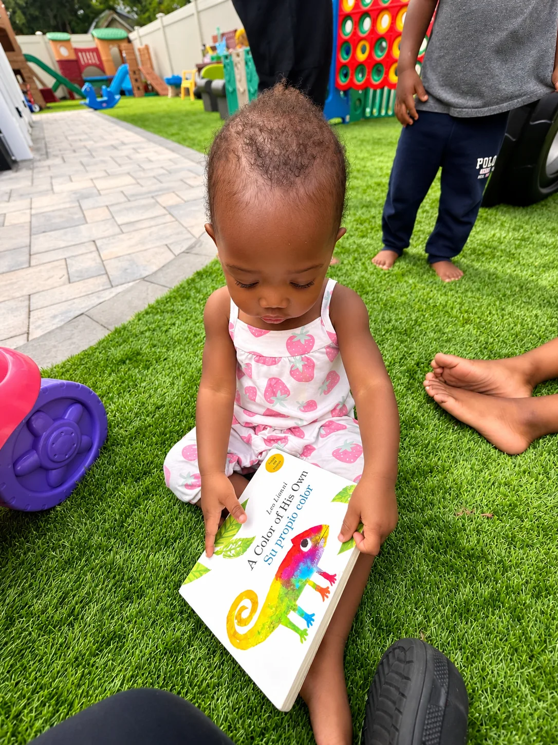 Toddler exploring colorful illustrated pages while seated on the grass outdoors