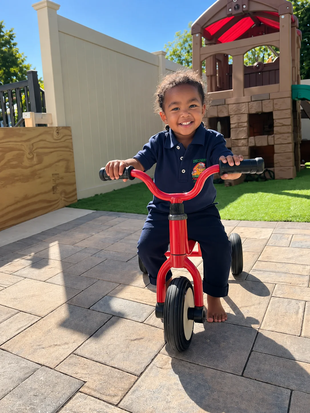 Smiling child riding a red tricycle in the outdoor play yard