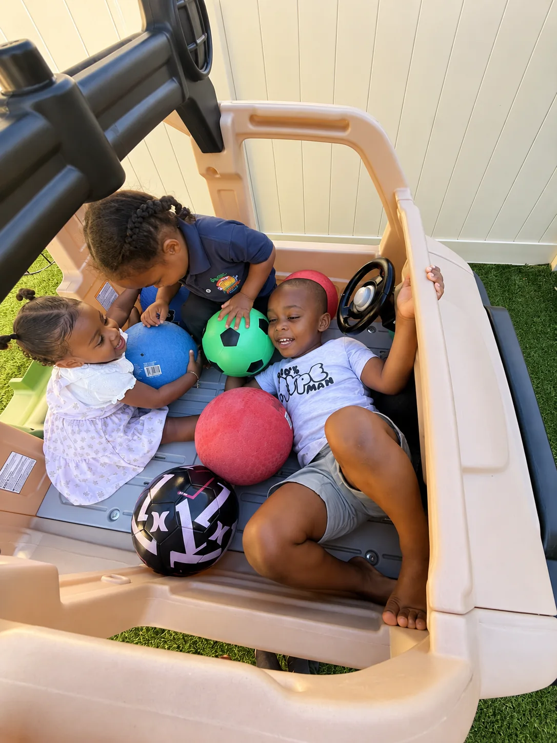 Three children playing together with colorful balls inside an outdoor play truck