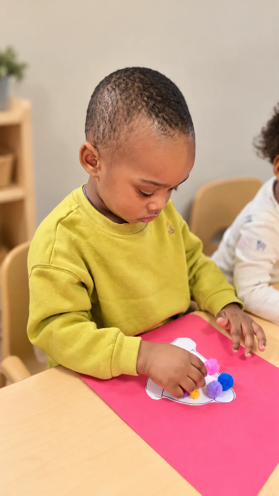 Preschool child arranging soft pom-poms on a paper shape during a table activity