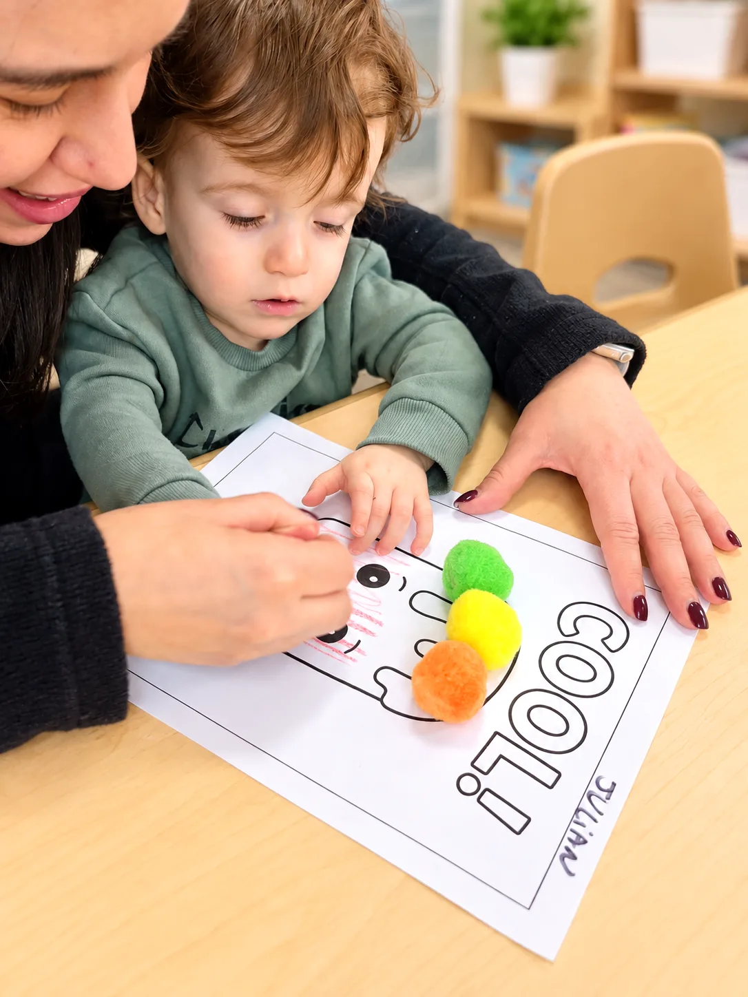 Teacher guiding a young child placing colorful pom-poms on a worksheet