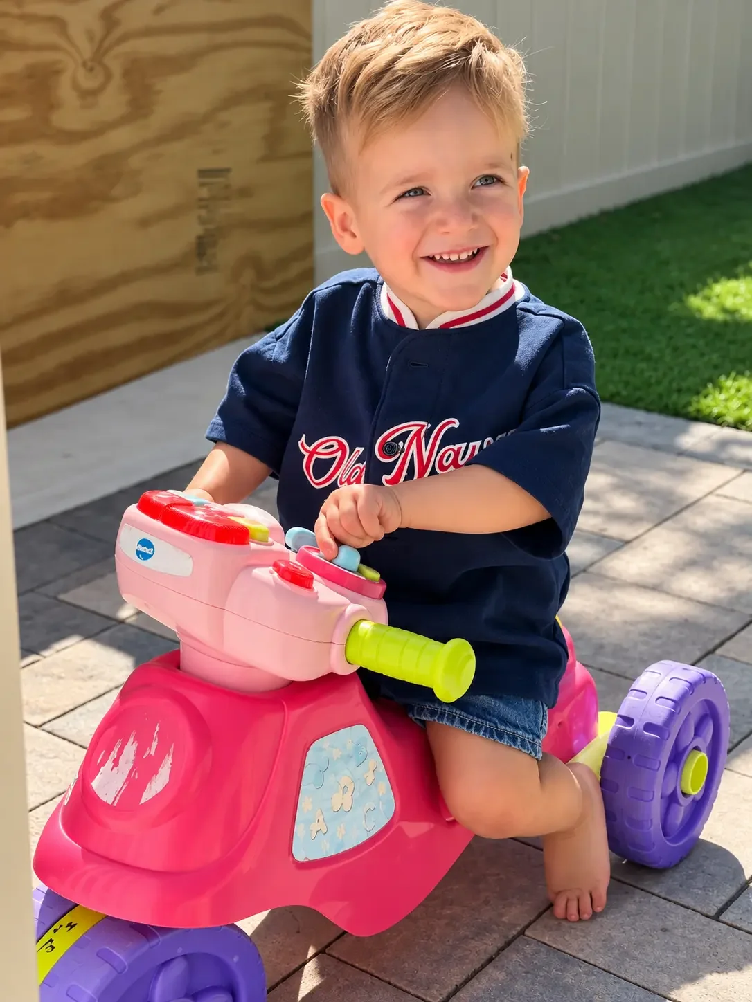 Smiling child riding a colorful toy tricycle outdoors