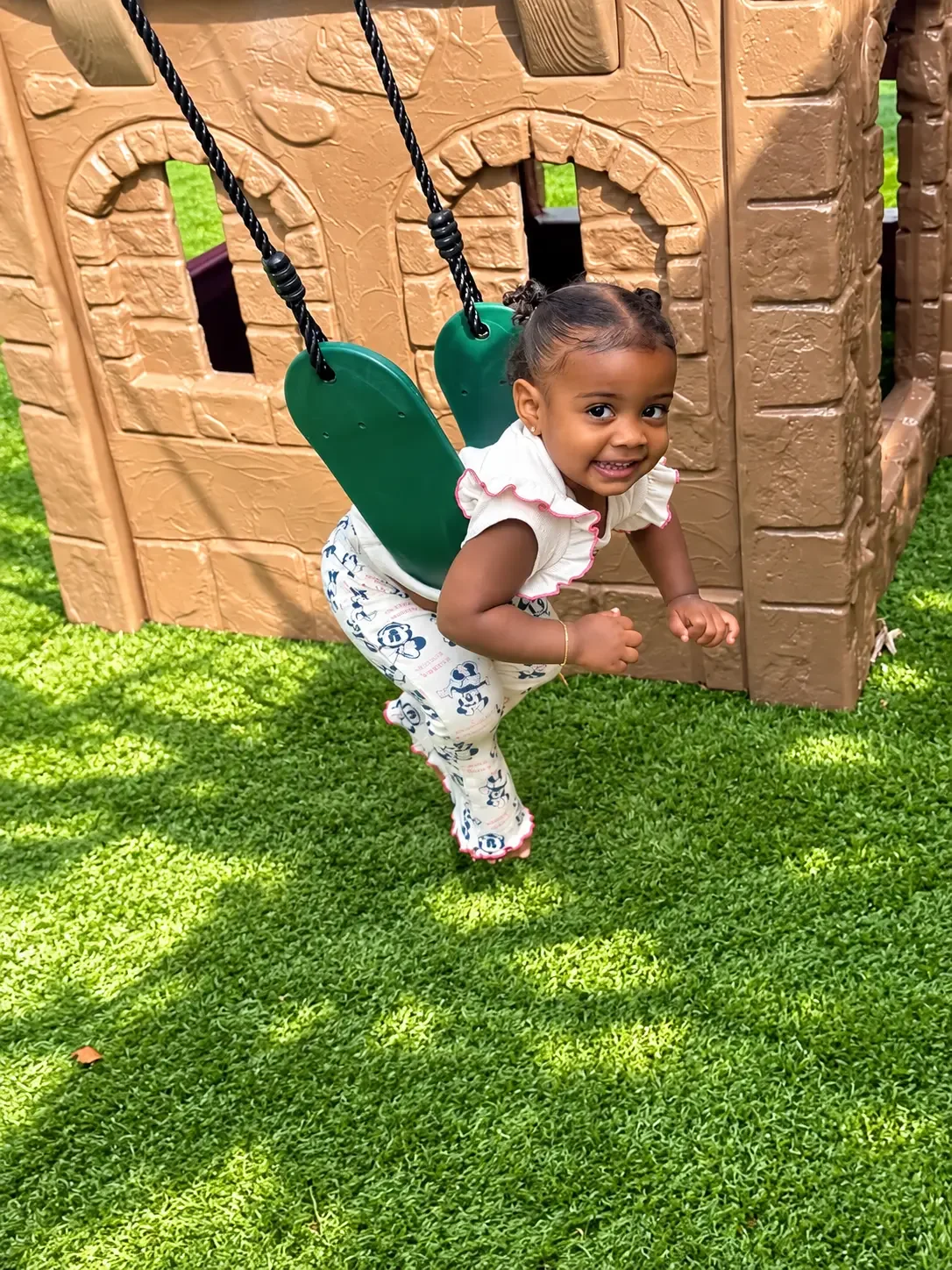 Smiling toddler enjoying a bucket swing in the play yard