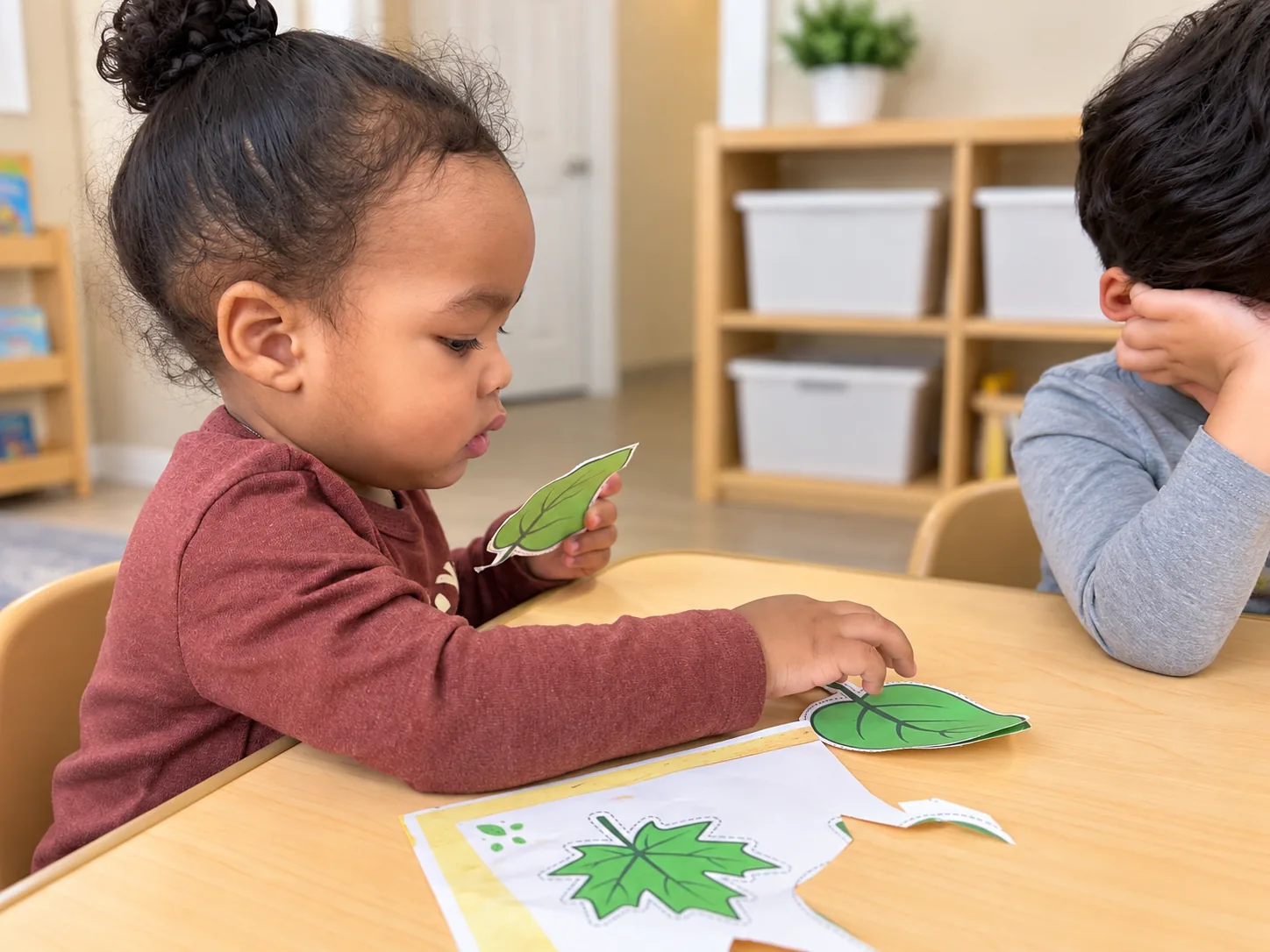 Young child matching green paper leaf cutouts during a table activity