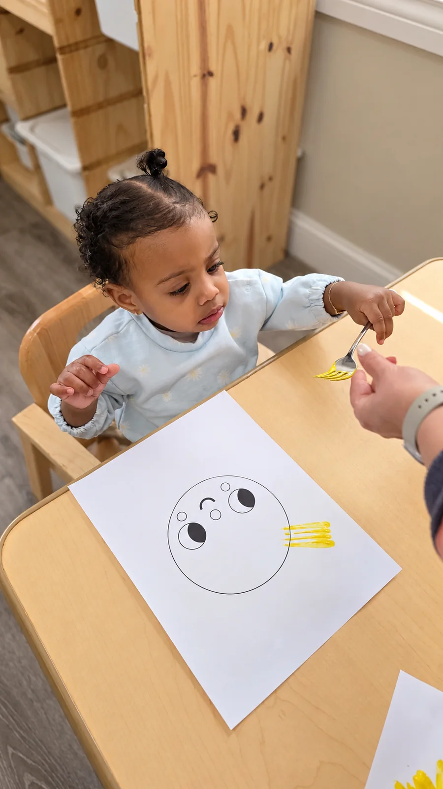Toddler using a fork to paint a cheerful sun during a hands-on art activity