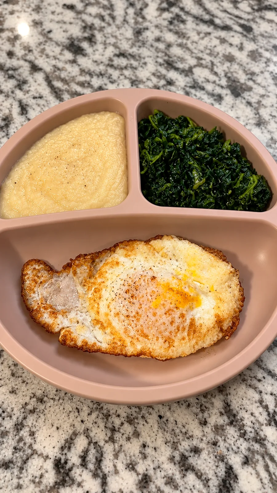 Fried egg, grits, and sautéed spinach served in a divided meal tray